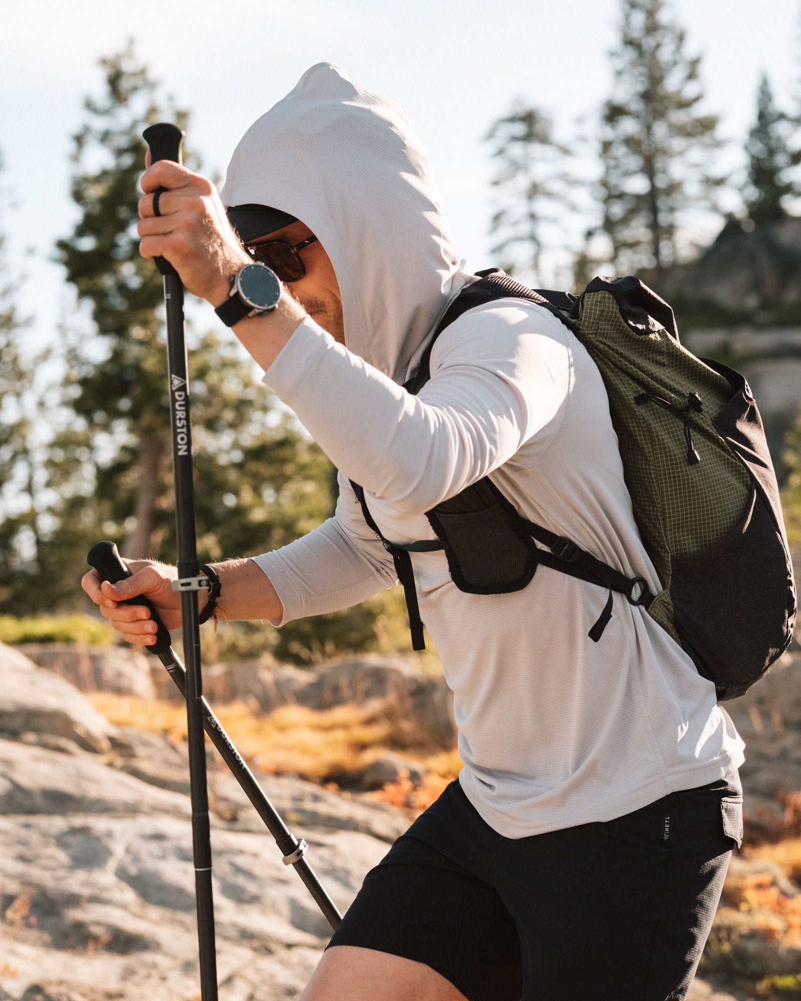 Man hiking through the mountains with trekking poles wearing a KETL Nofry Sun Hoodie.