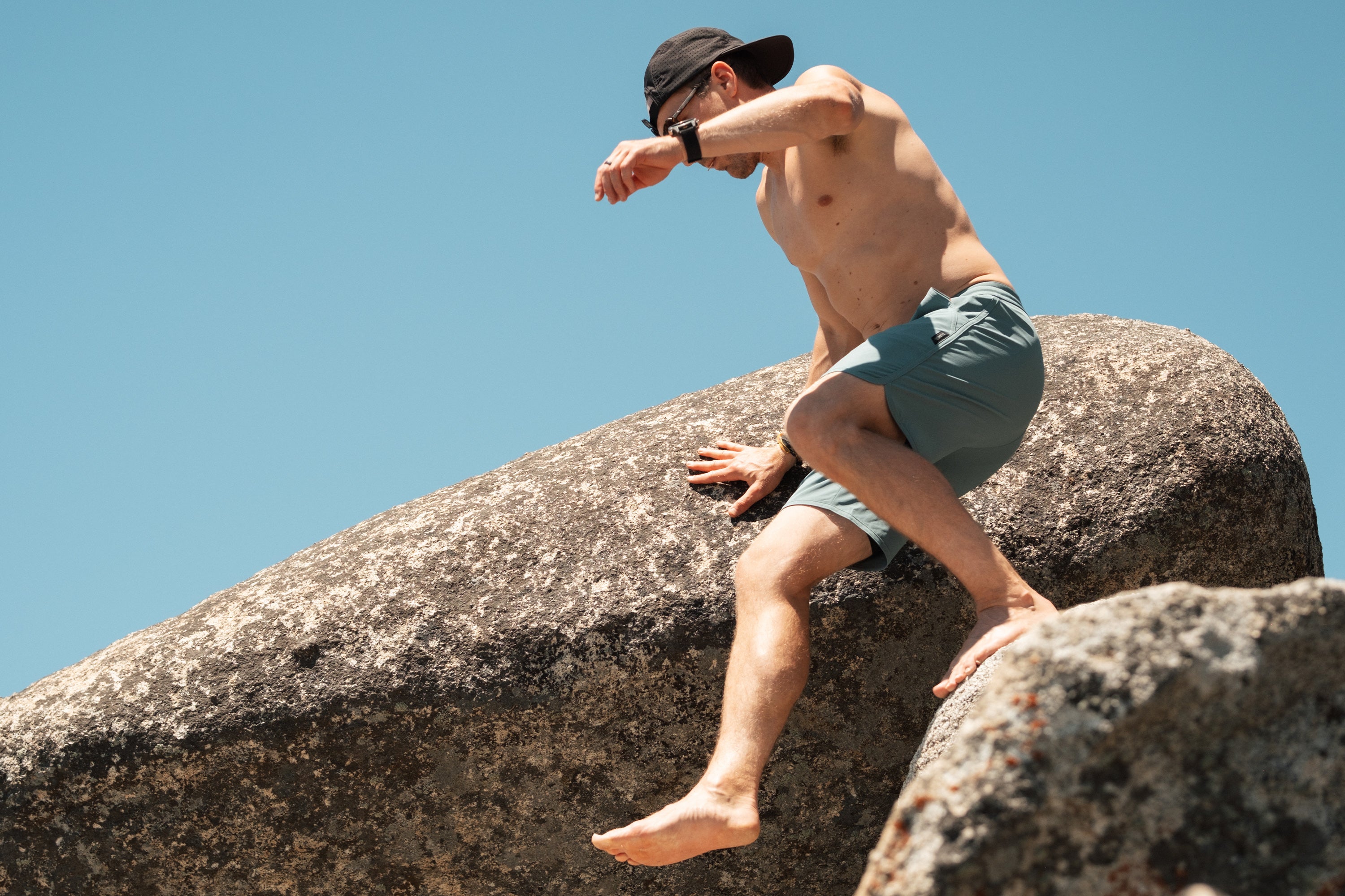 Man wearing teal Alpine Dip boardshorts scaling rocks.