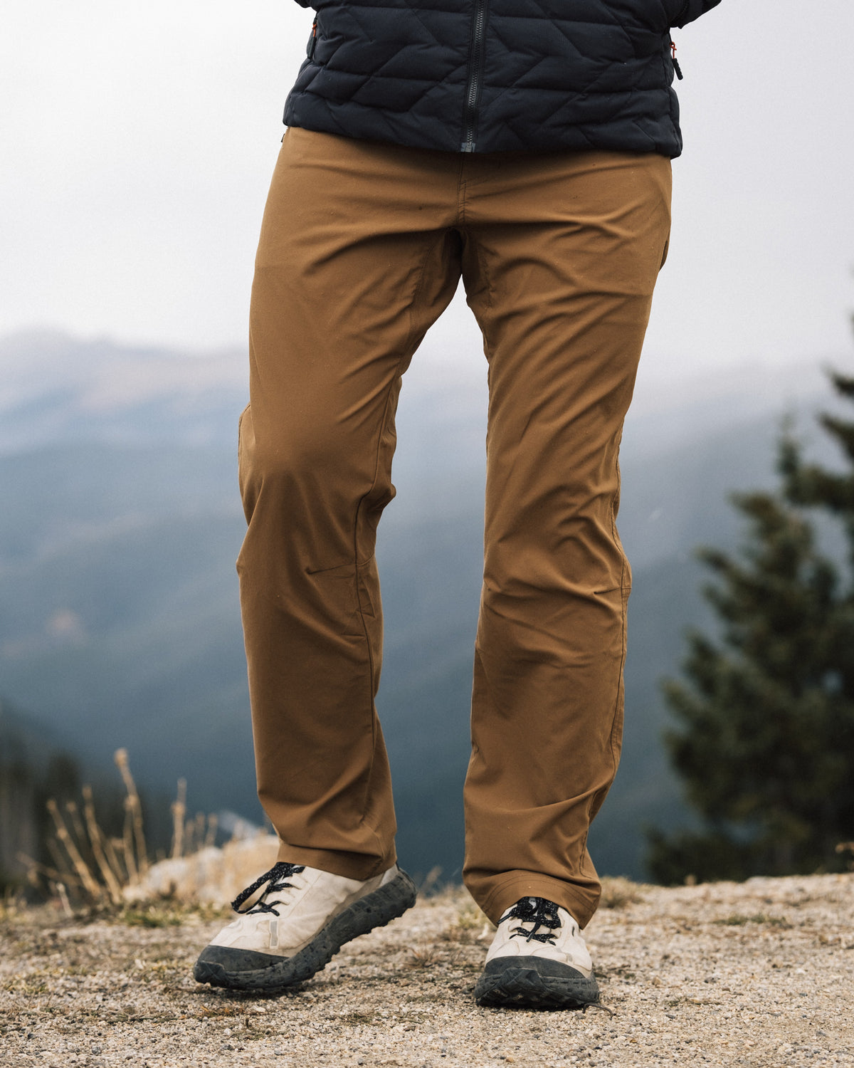Model wearing Ketl Mountain Apparel Shenanigan Outdoor Pants Straight Fit in brown, standing outdoors showing full front fit and rugged style
